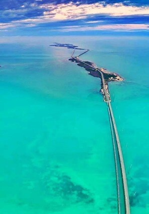 An aerial view of a coastal area with a long, narrow landform extending into the sea, connected to a larger landmass by a bridge. - Wake Up to City Views Pool Gym High Speed Wifi (Miami)