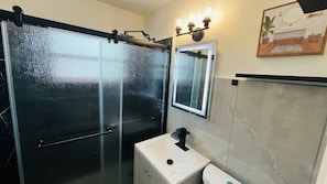 Une salle de bain avec une douche à parois de verre, un lavabo doté d’un robinet noir et un miroir au-dessus.
