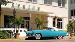 Um carro vintage azul-turquesa estacionado em frente a um prédio com a placa 'AVALON'.