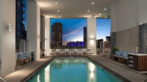 A modern indoor pool area with a cityscape view, lounge chairs, and a reception desk.