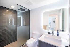 A modern bathroom with a glass-enclosed shower, a white toilet, and a large mirror above a white sink.