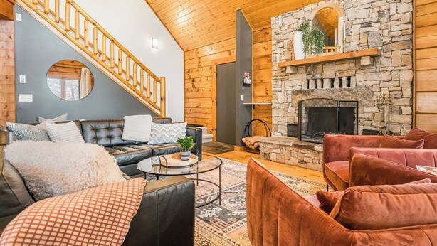 Una sala de estar acogedora con chimenea de piedra, sofás de cuero, una escalera de madera y un espejo redondo grande.