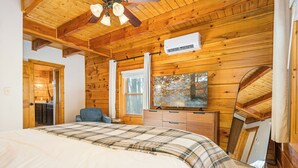 Un dormitorio de cabaña de madera con una cama, un tocador, una silla y un ventilador de techo.