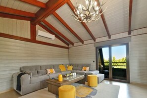 Relax in this stylish living room with a high ceiling, comfortable sofa, and glass door leading to a lush outdoor view.