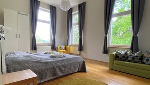 A bedroom with a bed, a green sofa, a round rug, a wooden table, and a window with curtains.