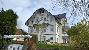 A large, two-story house with a stone entrance gate, a small garden, and a paved driveway.