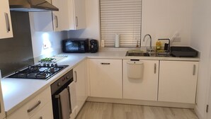 A compact kitchen with white cabinets, a gas stove, a microwave, and a sink. - Charming & Spacious 3-Bed Family Home in Heart of Romsey (Romsey)