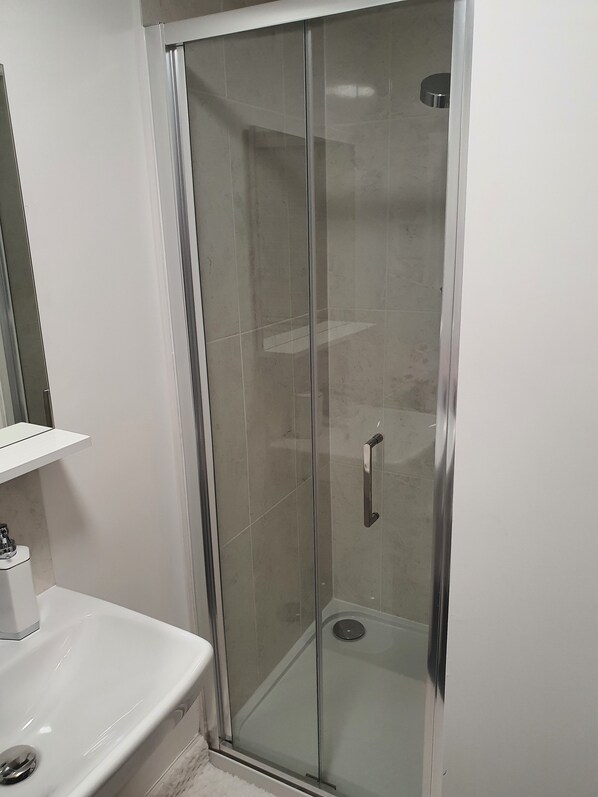 Un box de ducha con paredes de cristal, un lavabo blanco y un espejo encima.