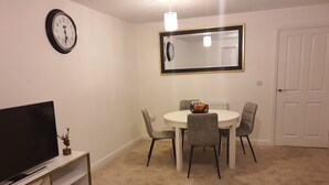 A dining area with a round table, four chairs, a television on a stand, and a large mirror on the wall. - Charming & Spacious 3-Bed Family Home in Heart of Romsey (Romsey)