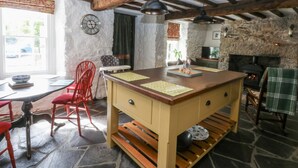 A rustic kitchen with a large island, stone walls, exposed wooden beams, and a stone fireplace.