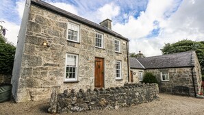 A stone building with a wooden door, multiple windows, and a gravel driveway.