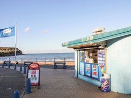 A seaside ice cream shop with a signboard, a beach in the background, and a flag.