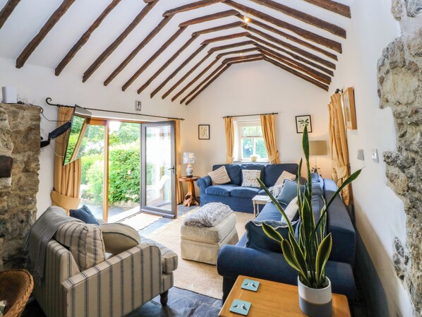 A cozy living room with a blue sofa, a striped armchair, and a wooden coffee table. There is a potted plant on the table and a television mounted on the wall. - Tyddyn Iolyn (Tyn-y-Gongl)