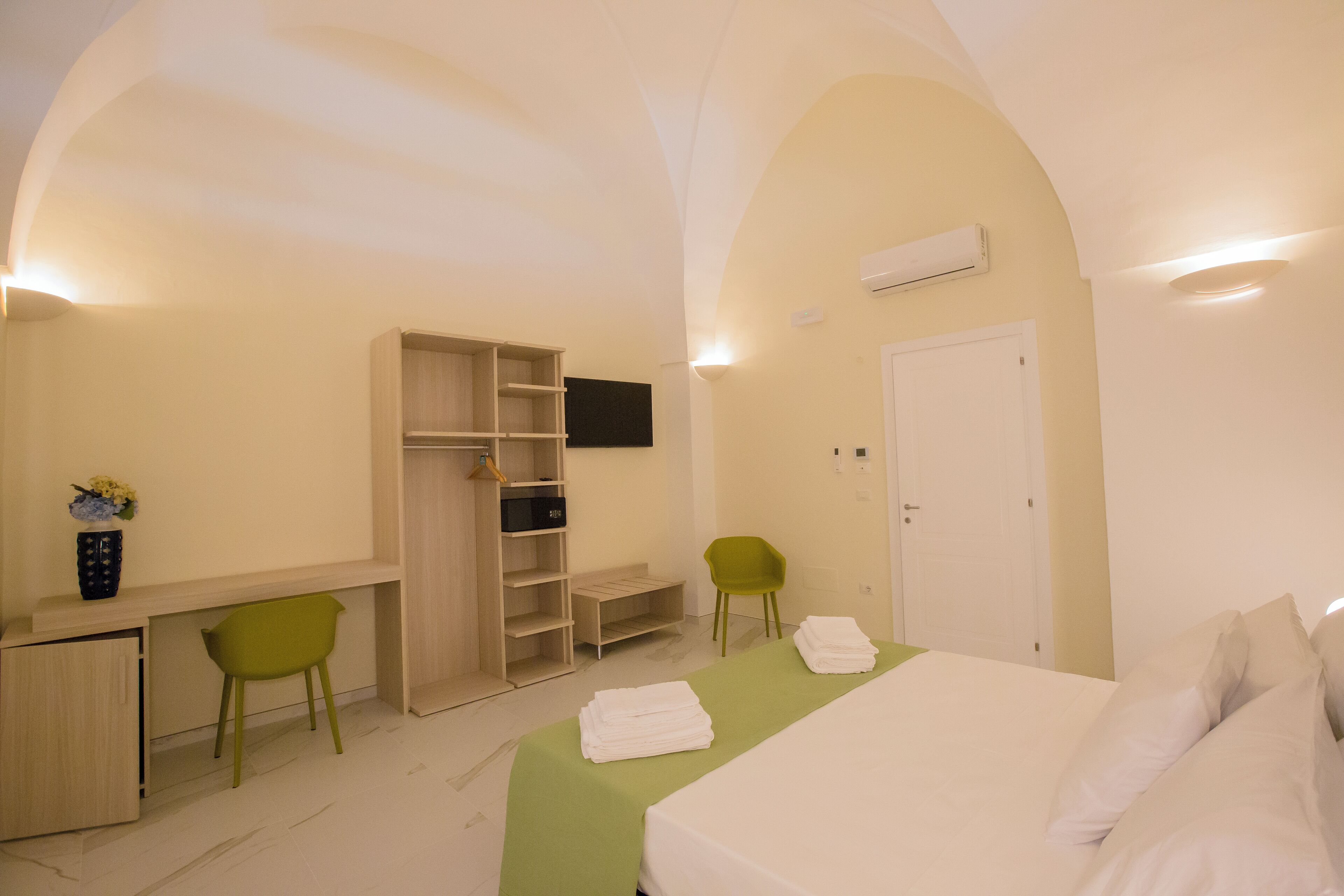Une chambre d’hôtel avec un lit, un bureau, une armoire et une chaise verte.