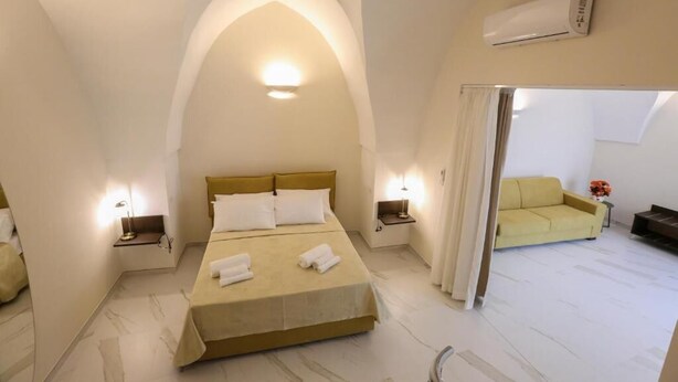 A hotel room with a bed, two bedside tables, a sofa, and an air conditioning unit. - LE DUE DIMORE (Collepasso)
