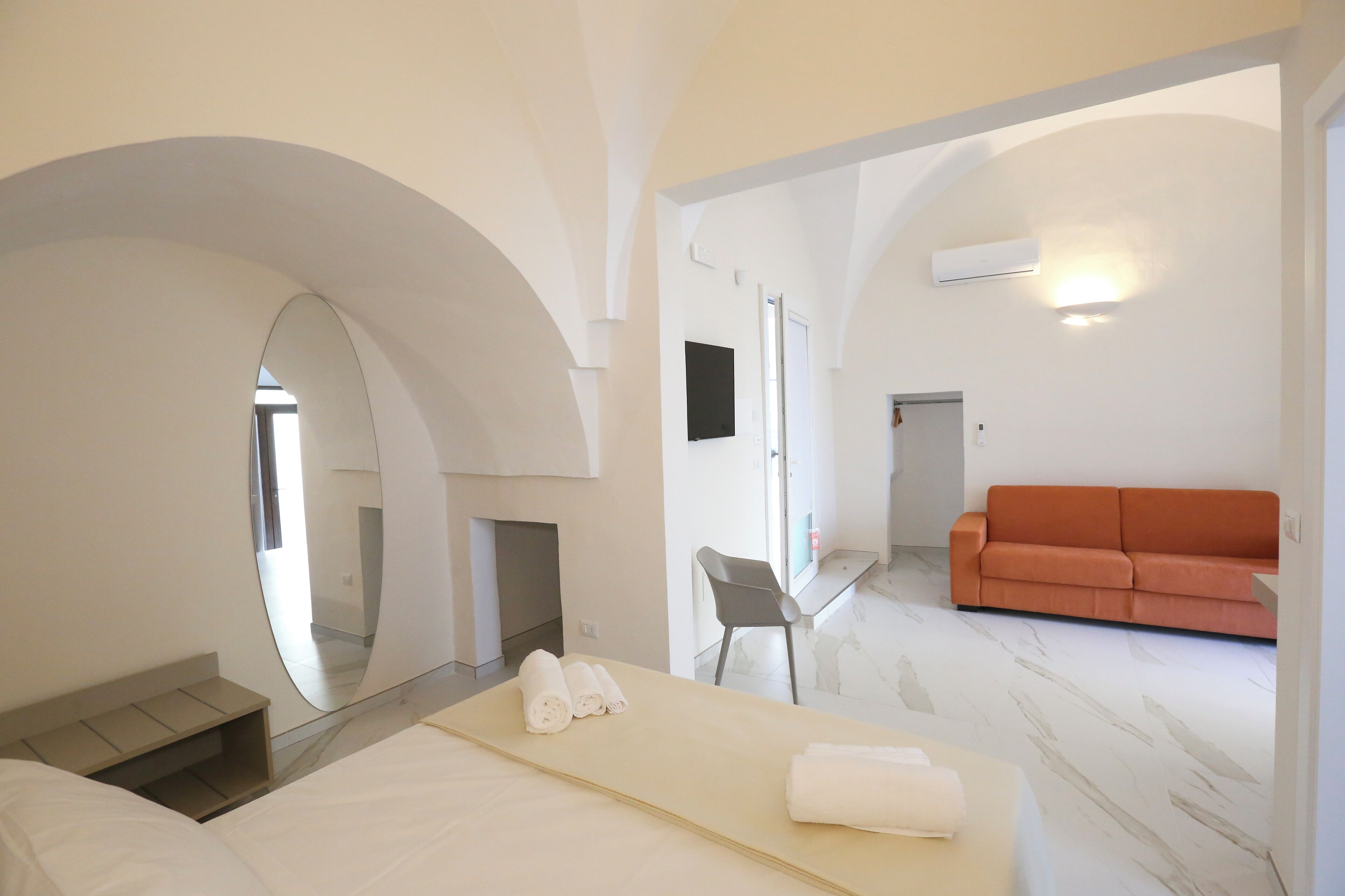 Ein modernes Hotelzimmer mit Bett, einer Couch, einem Spiegel und einem Sessel.
