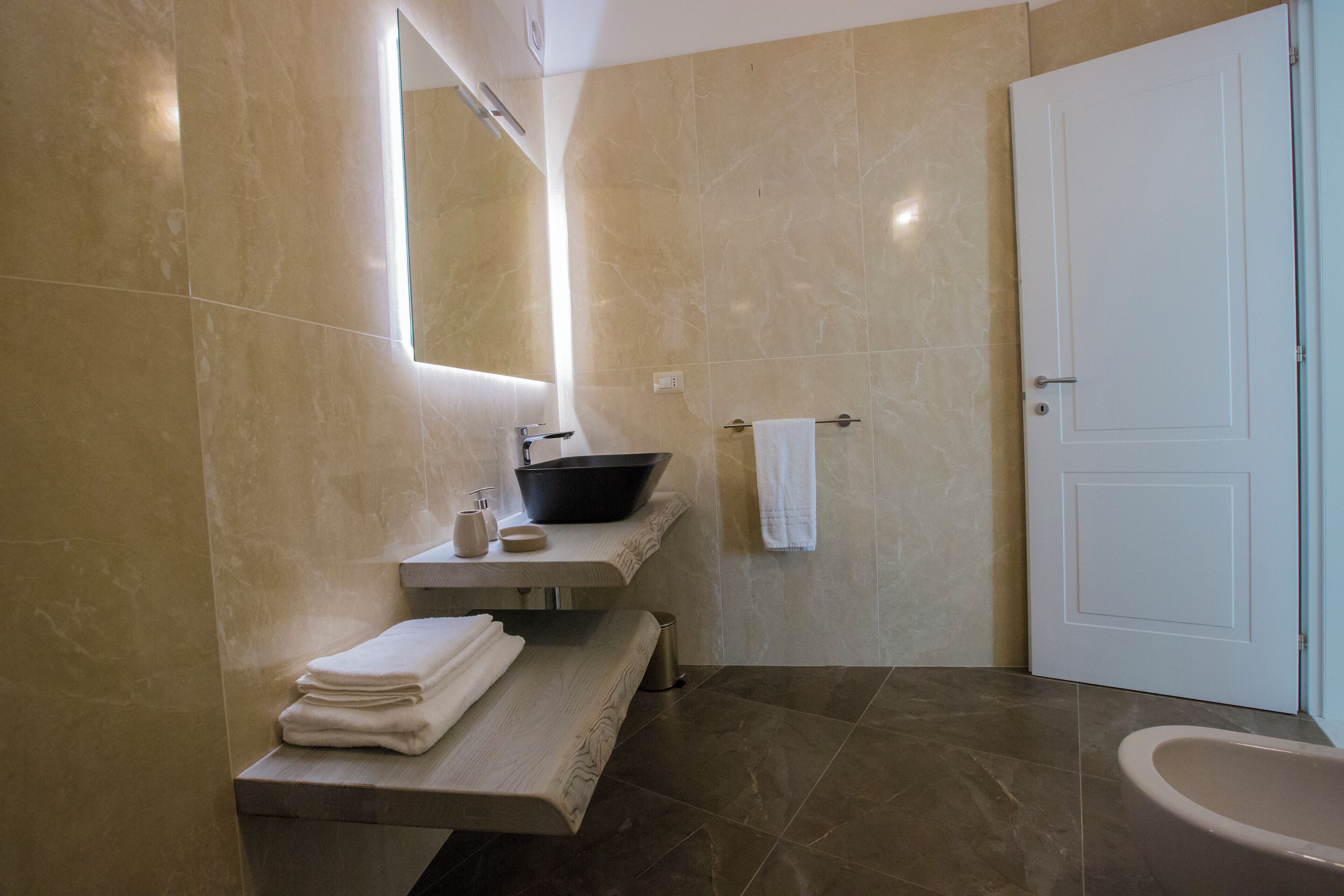 A modern bathroom with a large mirror, a black sink, a toilet, and a towel rack.