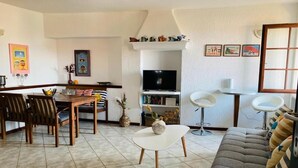 A living room with a sofa, dining table, chairs, a TV, and a bookshelf.