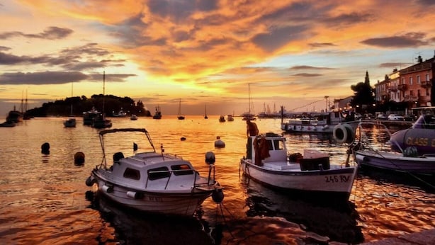 A harbor at sunset with boats docked, a bridge in the background, and buildings along the shore.
