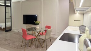 A modern kitchen with a white countertop, a built-in oven, and a microwave. There is a dining area with a glass table and four chairs, one of which is red. A flat-screen TV is mounted on the wall above the dining area. - Luxury 2BR apartment in the center (Yerevan)