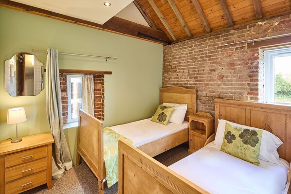 A bedroom with two wooden beds, a nightstand, a mirror, and a window with curtains.