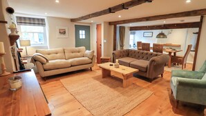 A spacious living room with a wooden floor, two sofas, a coffee table, and a dining area with wicker chairs. - 8 1/2 Church Street (Ambleside)