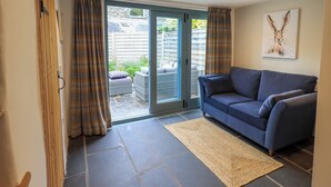 A living room with a blue sofa, a woven rug, and a sliding glass door leading to a patio with outdoor furniture. - 8 1/2 Church Street (Ambleside)
