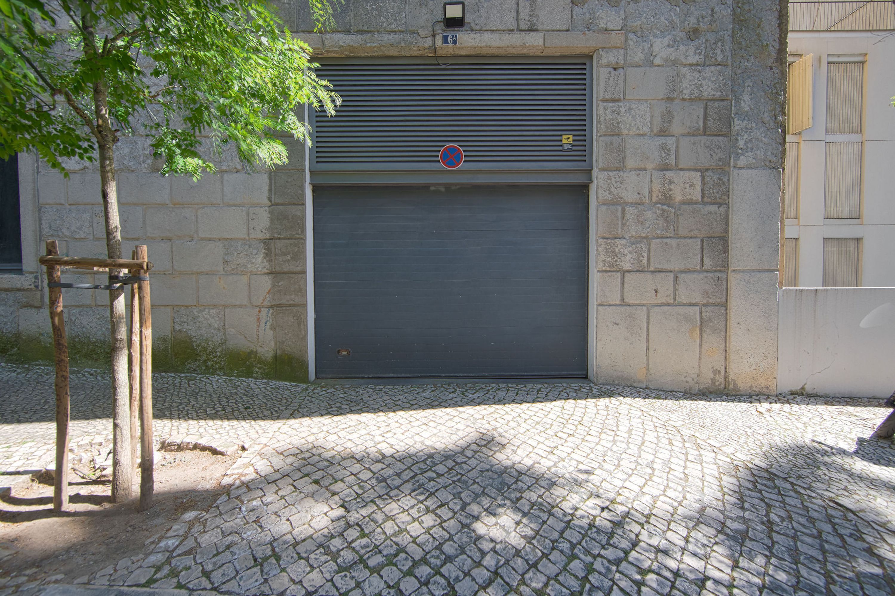 Une rue pavée avec une porte de garage en métal fermée et un arbre sur le côté gauche.