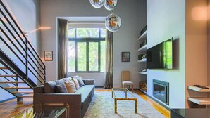 Una sala de estar moderna con un sofá, una mesa de centro de vidrio, una chimenea, un televisor y una escalera.