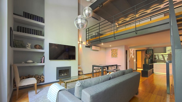 Una sala de estar moderna con un sofá gris, piso de madera, una chimenea y un televisor montado en la pared.