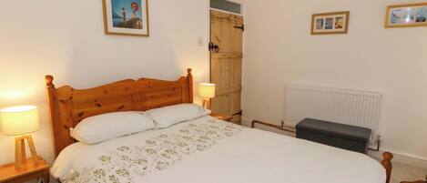 Un dormitorio con una cama de madera, una mesita de noche con una lámpara, un radiador y una puerta que da a otra habitación.