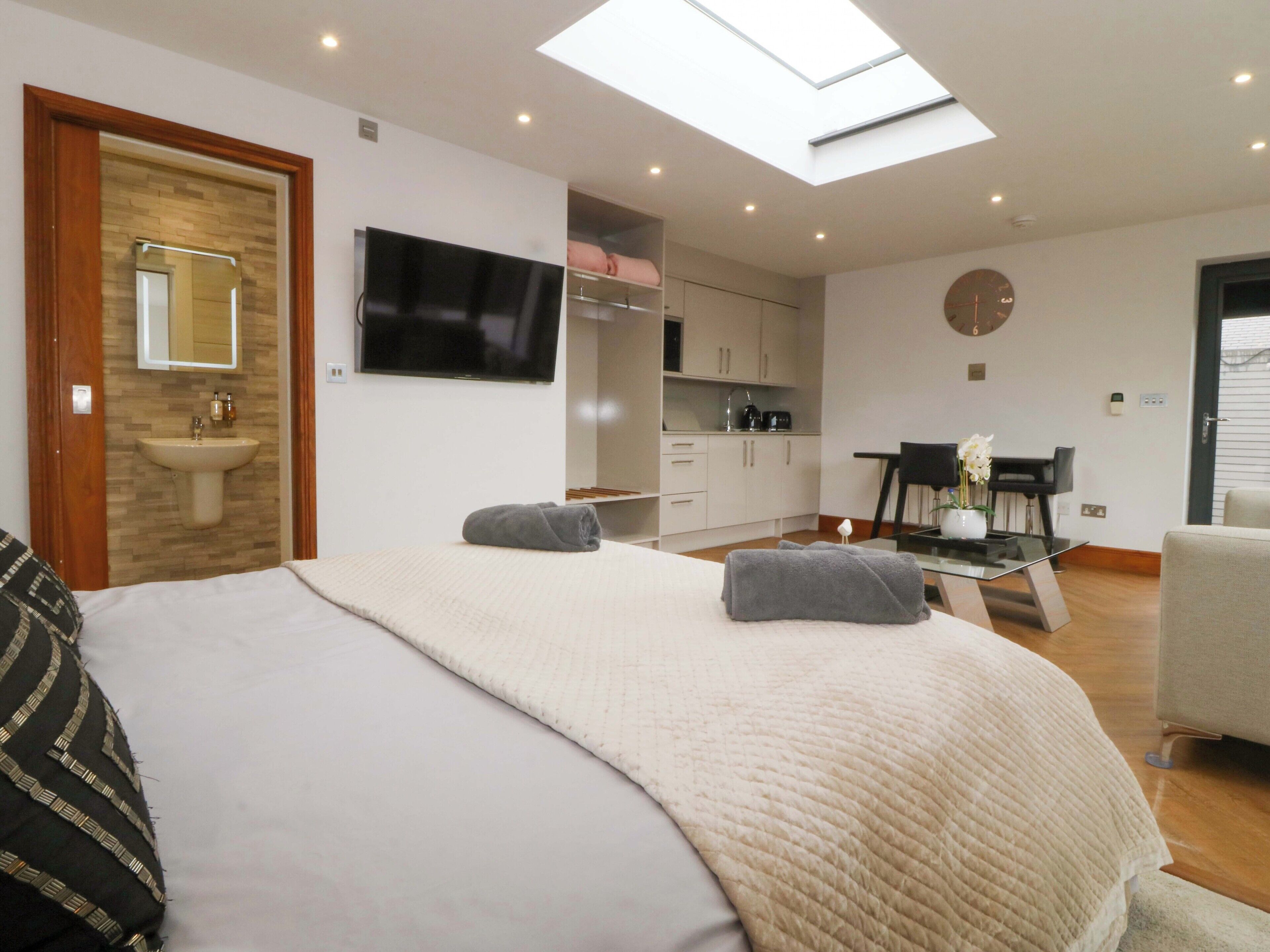 A modern bedroom with a bed, a skylight, a TV, a bathroom, and a dining area.