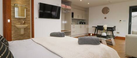 A modern bedroom with a bed, a skylight, a TV, a bathroom, and a dining area.