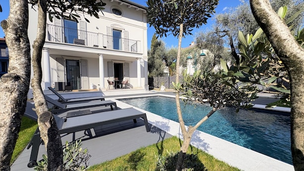 Un espace aménagé au bord de la piscine, avec des chaises longues et un bâtiment blanc doté de balcons.
