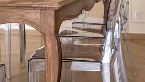 Ein Esstisch mit einer Glasvase, die Pflanzen enthält, umgeben von transparenten Plastikstühlen.