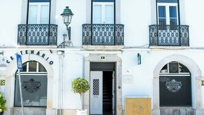Ein Gebäude mit weißer Fassade, einem Ziegeldach und drei Balkonen mit schmiedeeisernen Geländern.