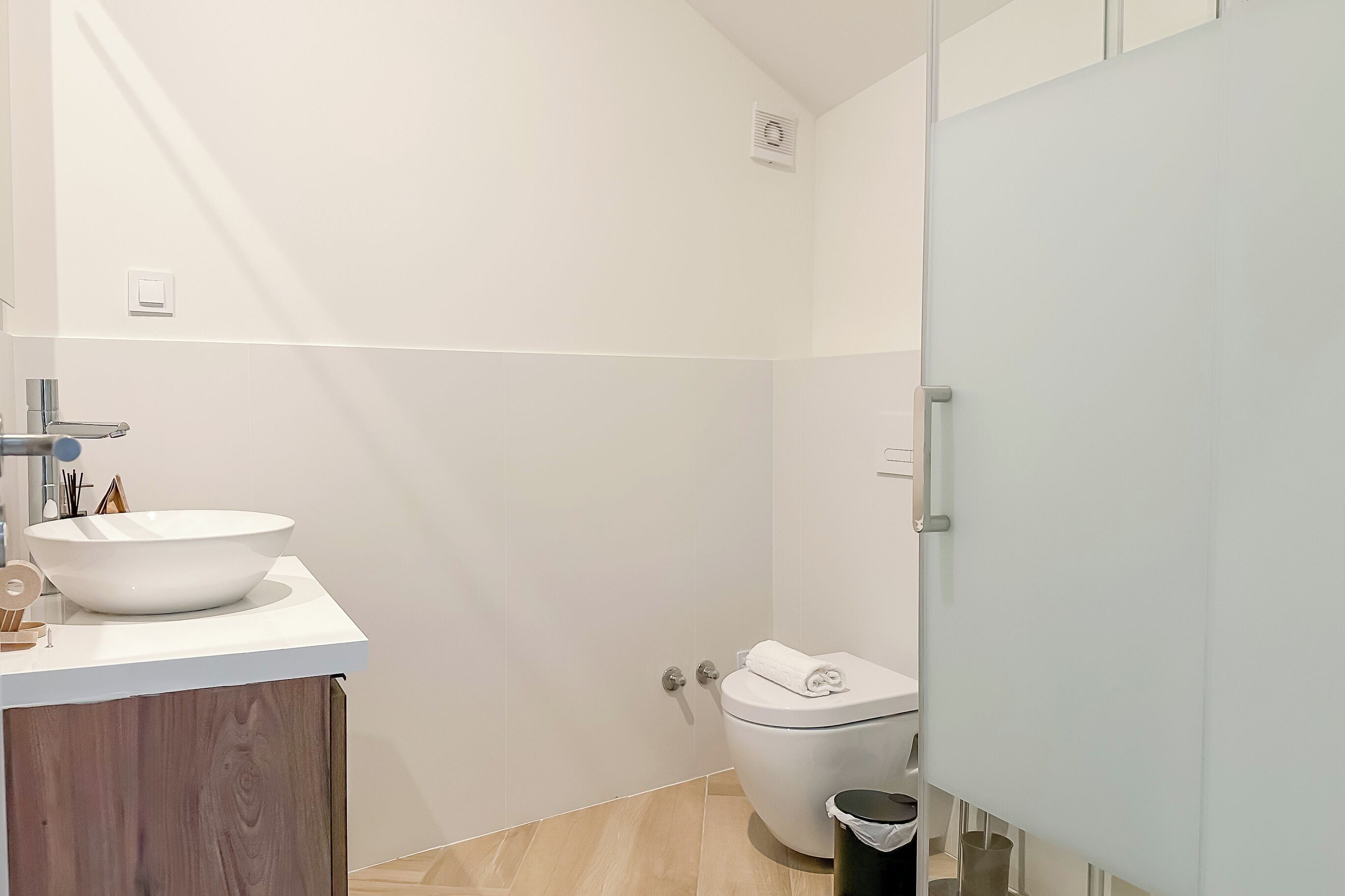 A modern bathroom with a white sink, toilet, and a wooden vanity.