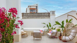 Eine Dachterrasse mit Korbmöbeln, Topfpflanzen und einem Hängesessel.