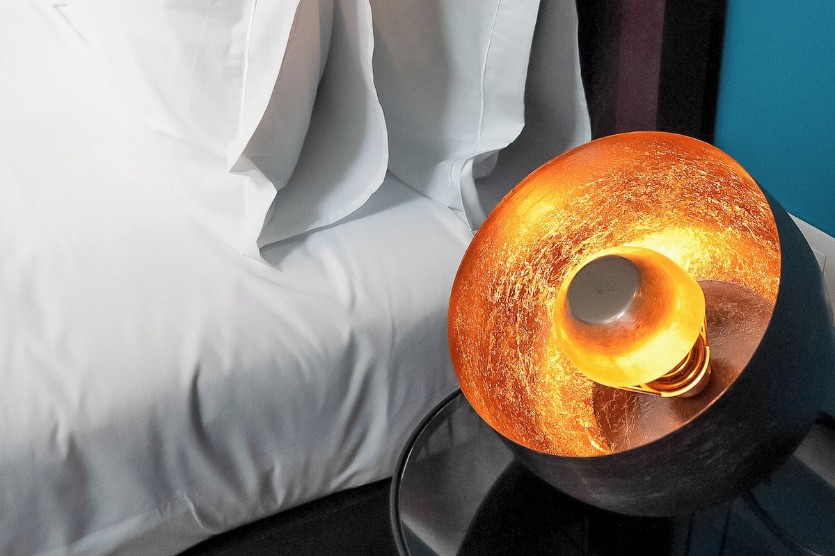 A bed with white bedding and a unique, textured lamp with a warm light.