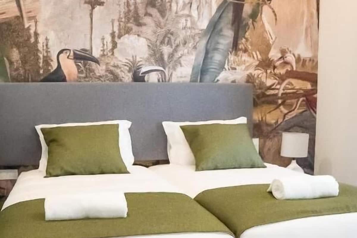 A double bed with green and white bedding, a grey headboard, and a mural of a jungle scene on the wall behind.