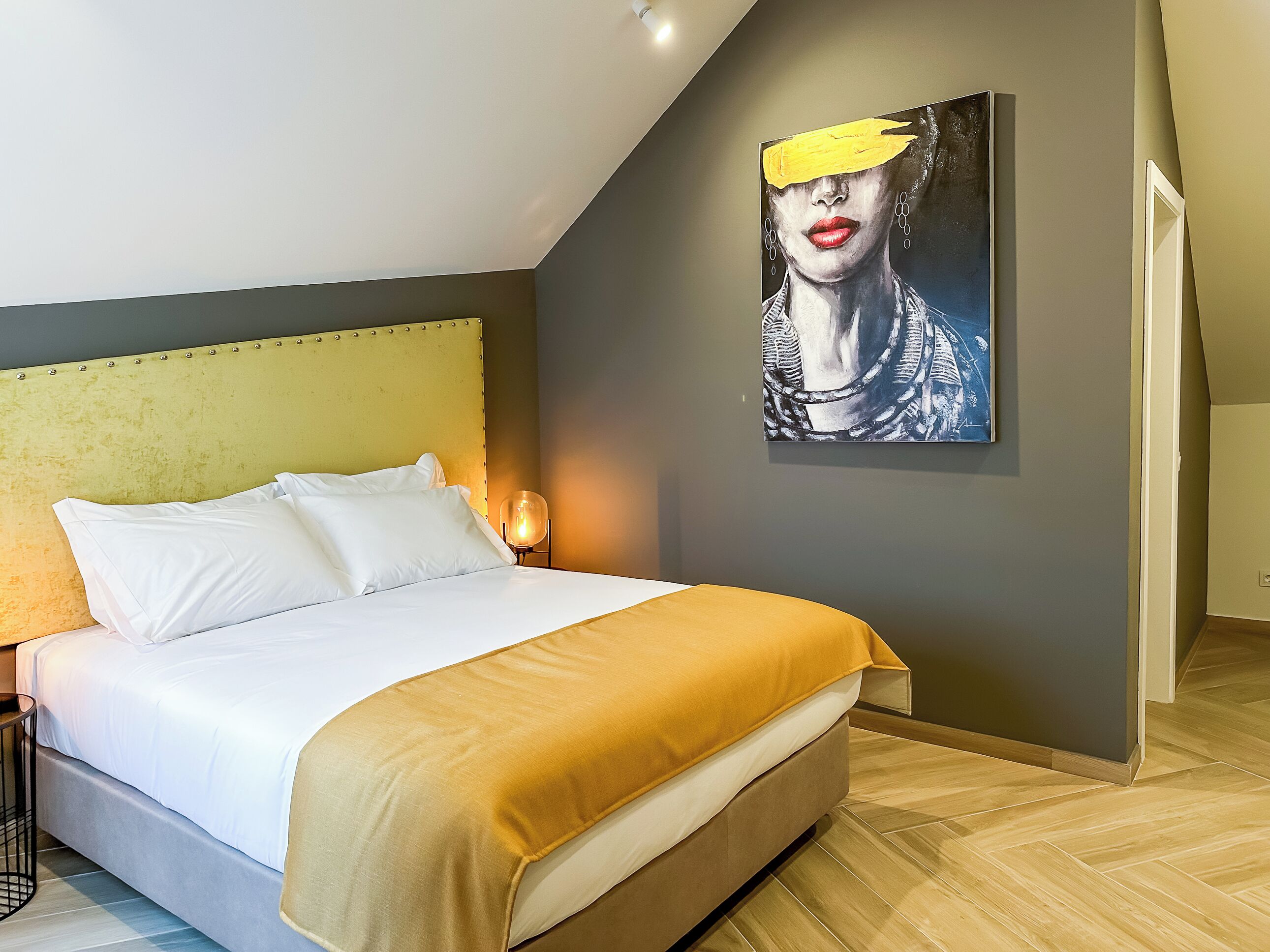 A modern bedroom with a bed, a headboard, a wall-mounted painting, and a nightstand.