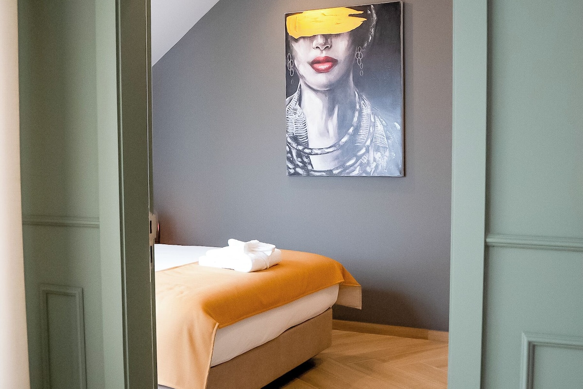 A bedroom with a bed, a painting on the wall, and a wooden floor.