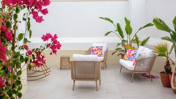 A patio with wicker furniture, potted plants, and a white wall.