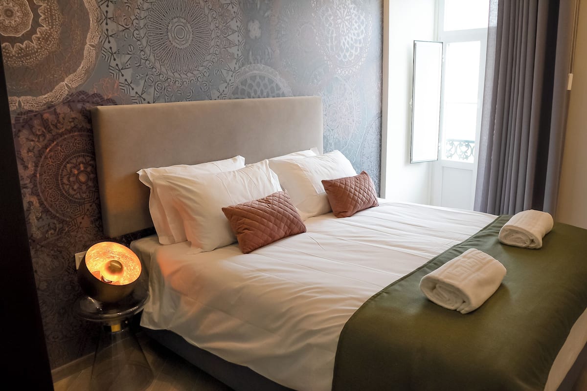 A neatly made bed with white linens and two pillows, a bedside lamp, and two towels on the bed.