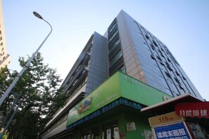 Un edificio de varios pisos con fachada verde y señalización que indica un establecimiento comercial o de servicios.