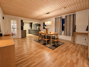 A modern kitchen with wooden cabinets, a dining area with a table and chairs, and a view of the living room. - Modern 3BR Villa w/ Sauna, Garden & Fast WiFi – 1hr from Copenhagen (Ruds-Vedby)