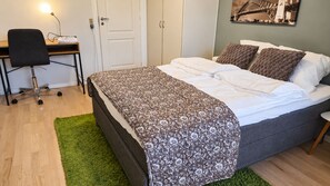 Une chambre à coucher avec un lit, un bureau et une chaise, un tapis vert et une porte.