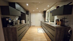 Een moderne keuken met donkere kastjes, een houten vloer en een centraal kookeiland met spoelbak en aanrecht.