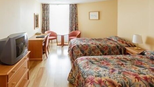 Una camera d'albergo con due letti, una scrivania, una sedia e una televisione.