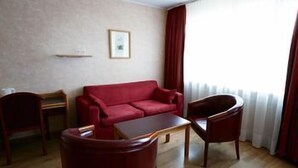 Ein Zimmer mit einem roten Sofa, einem Holztisch, zwei Holzsesseln, einem kleinen Tisch und einem gerahmten Bild an der Wand.